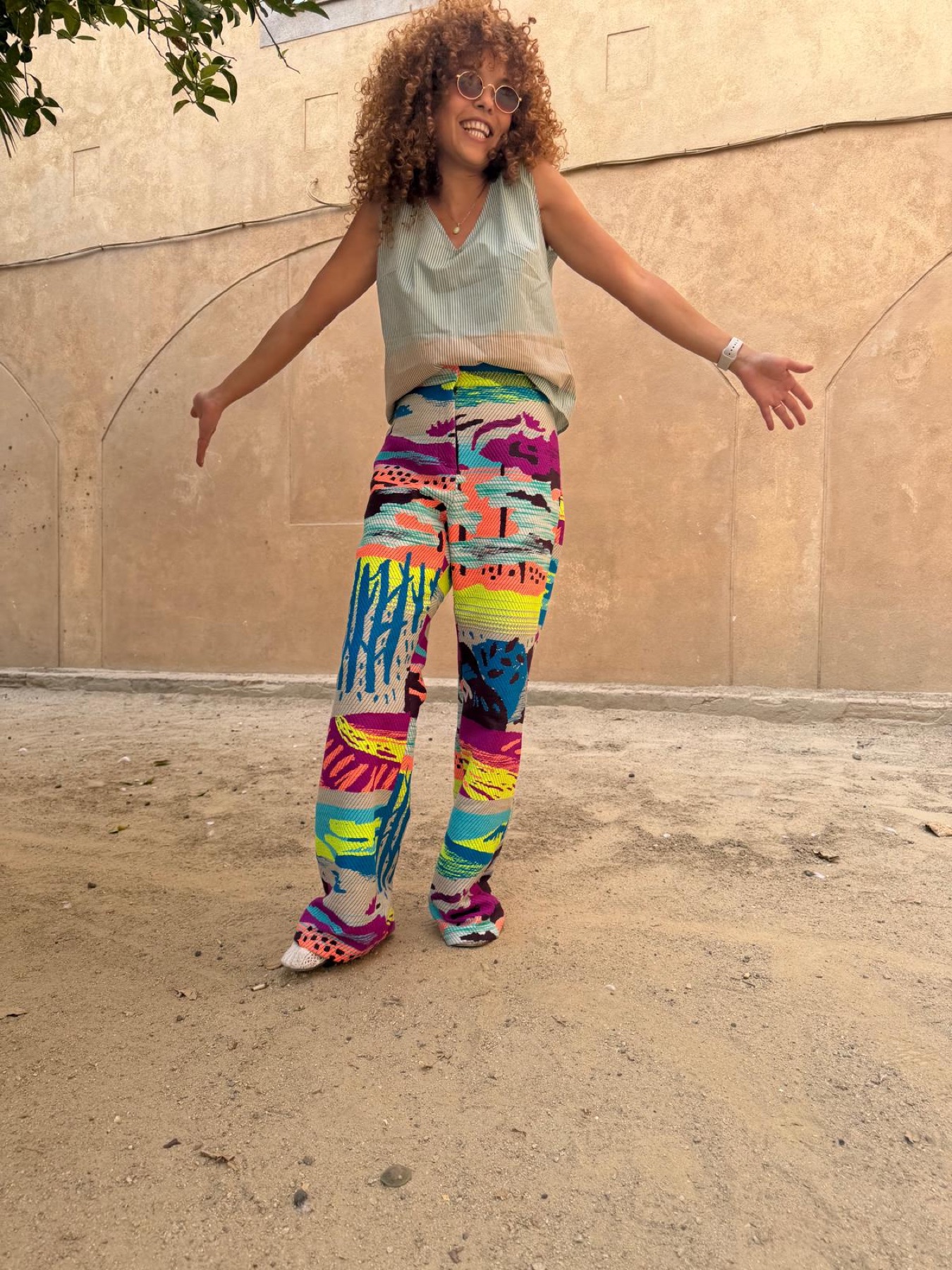 Scan 15 — landscape tapestry pants and sage tank, arms open against Ibiza stucco