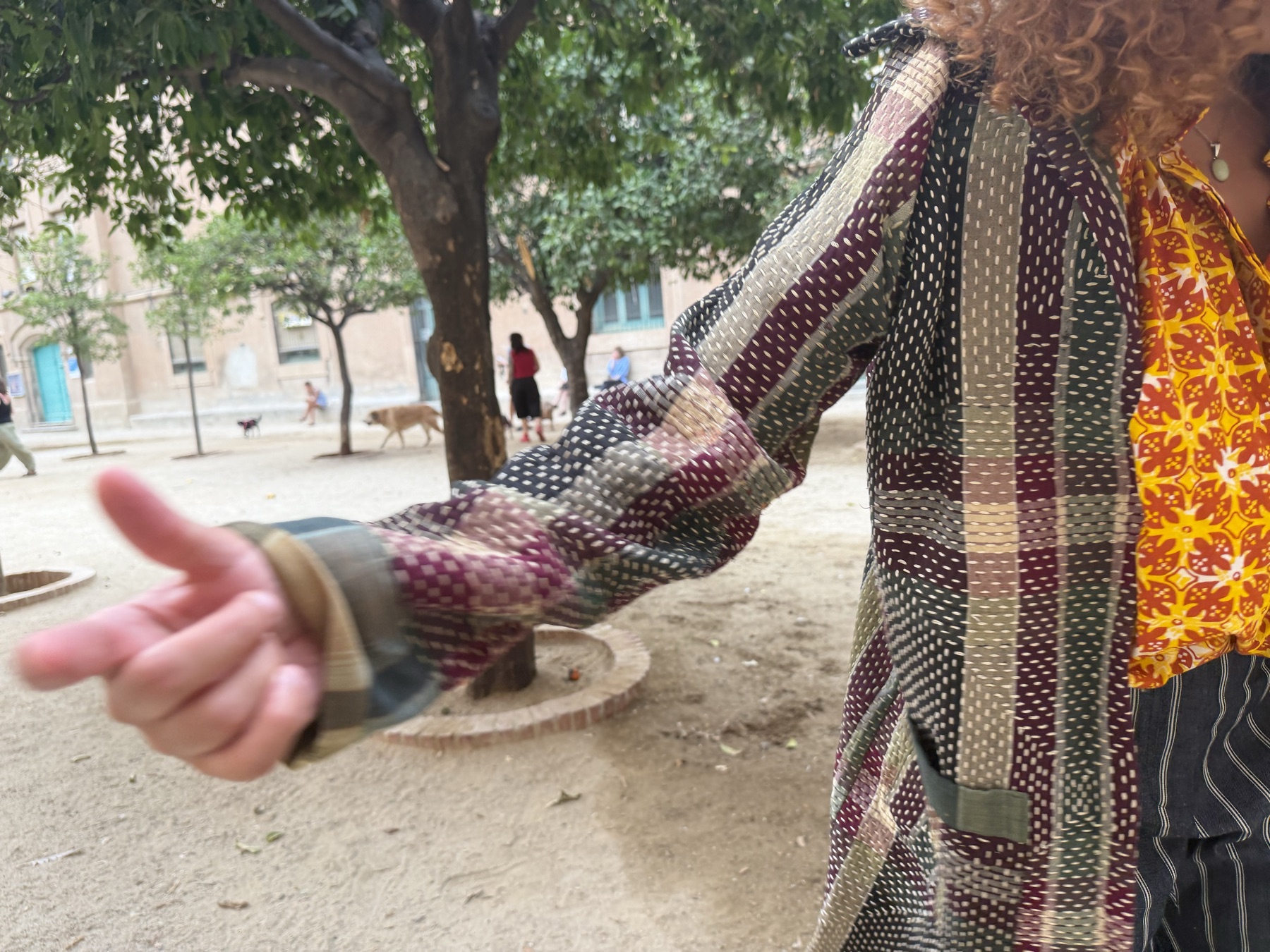 Chromatic kantha grid duster in motion — arms open, courtyard light